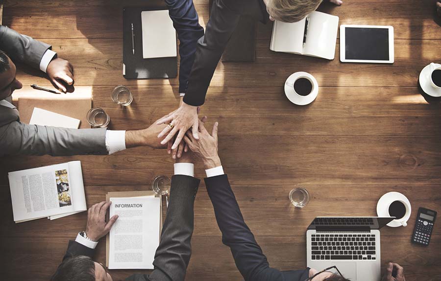 image of 4 professionally dressed hands placed together atop a wooden table.